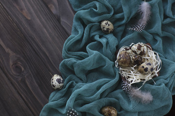 Easter decoration feathers quail eggs, green fabric on wooden brown background.