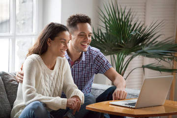 Happy young couple laughing watching funny video or comedy movie online, cheerful man and woman...