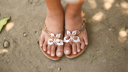 Tanned legs of a little girl in slates with a decorative butterfly. Girl barefoot in summer shoes...