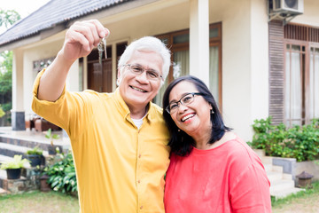Obraz premium Portrait of a happy senior man posing with his wife while holding the keys of a residential house 