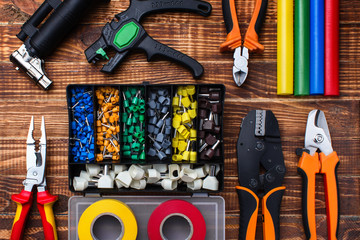 background of professional electrician tools: cable lugs in the organizer box, insulating tape, earplugs, cutters, tips, burnerpuller insulation, on a wooden board