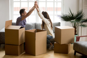 Excited couple holding hands happy to move into new home, young family celebrate moving day sitting...