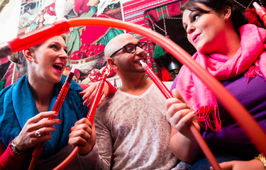 Women and man enjoying recreational shisha in hookah lounge on the weekend