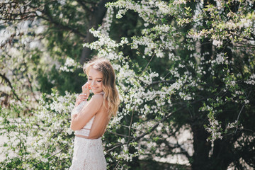 Beautiful young woman in a white romantic dress posing near blooming tree