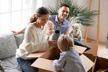 Happy family with two kids unpacking boxes after relocation moving into or settling in new home...