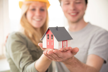 Junges Paar freudig lachend mit einem Modell-Haus, Eigenheim