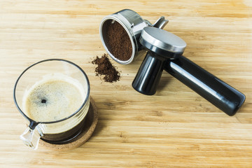 cup of espresso on wooden board with ground coffee