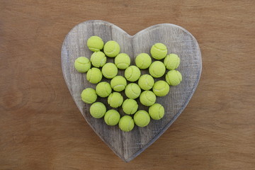Yellow tennis ball sweets on a wooden heart 