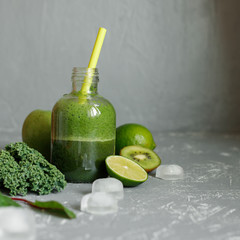 Healthy green smoothie with ingredients and ice cubes on gray background