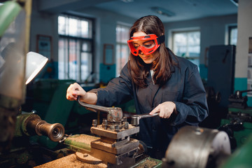Young woman student works on an automatic lathe CNC, industrial workshop. Concept vocational...