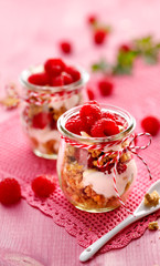 Granola with fresh raspberries and natural yogurt in a glass jar on a wooden pink table. Delicious breakfast or dessert. Healthy eating concept