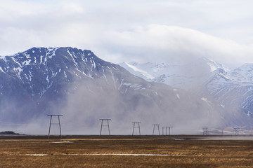 high voltage electric poles located in the countryside with snow capped mountain. The lines are...