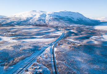 Aerial sunny winter view of Abisko National Park, Kiruna Municipality, Lapland, Norrbotten County, Sweden, shot from drone, with road and mountains