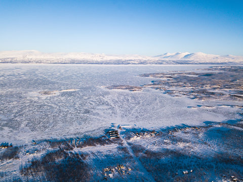 Aerial sunny winter view of Abisko National Park, Kiruna Municipality, Lapland, Norrbotten County, Sweden, shot from drone, with road and mountains