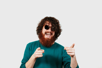 Happy excited bearded man in sunglasses pointing at the camera with two fingers isolated over white...