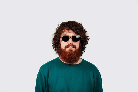 Portrait of hipster guy with curly hair wearing sunglases looking at the camera. fashion bearded male model posing isolated over white background.