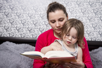 Young mother and little daughter read fairy tale books. Family concept. Spending time with children. Mom and daughter at home reading a book. The child listens to the story that mother reads.
