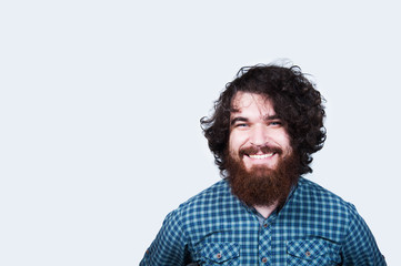 Obraz premium Smiling happy man with beard and curly hair on white background. Portrait of cheerful bearded hipster man. Young man looking confident at the camera.