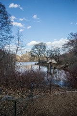New York, NY / USA - March 2016: a view on the pond and a wooden arbor in the Central Park, blue sky and bare trees, spring landscape
