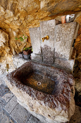 Natural water source in the mountains. Ancient water pipe carved into the rock. Holy spring  with pure cold water.