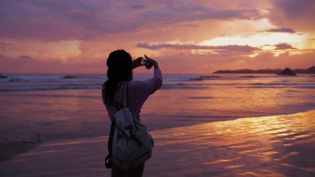 Girl takes a photo of beautiful sunset by the ocean.