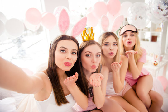 Self portrait of cheerful, pretty, attractive, charming, cute, sexy girls with bunny ears, crown, eye-mask on head shooting selfie on front camera, sending air kisses palm, enjoying meeting indoor