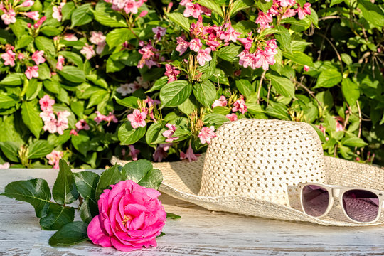 Pink rose, sunglasses, hat on the table in the garden