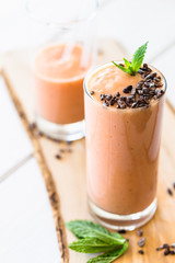 Vegan Papaya Smoothie Banana Milkshake Cacao Nibs and Mint on top on White Wooden Background