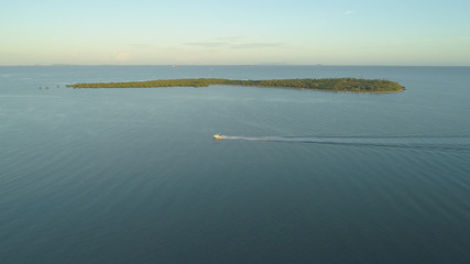 AERIAL: Small fishing boat leaves a trail in blue ocean water as it passes islet
