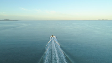 AERIAL: Fishing boat leaves a trail in ocean water as it speeds towards horizon.