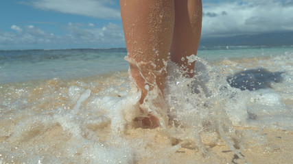 CLOSE UP: Stunning blue waves wash young woman's sandy legs on tropical beach.