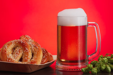 Pint of beer with ingredients for homemade beer on red with pretzel