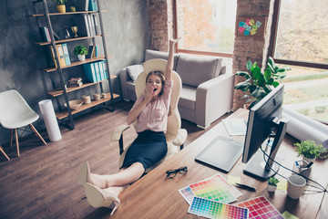 Pretty, attractive, drowsy, somnolent woman putting legs on desk, stretch herself, holding hand near mouth, stand up early for work, sitting on armchair in work station