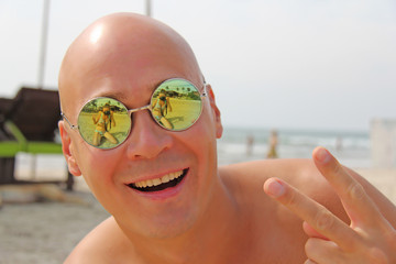 Bald man in mirror sunglasses. A beautiful tanned man on vacation, smiling. Portrait of a man close-up. Palm trees and the beach are reflected in the glasses. Reflection in glasses