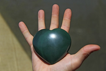 The hand holds the heart from natural stone green jade. Heart in hand. A stone in the shape of a heart. Love talisman, zen, spa