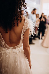 close-up of a girl in a white wedding dress with feathers and curly dark hair that stands with her...