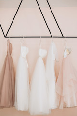 Five wedding dresses beige, white with lace and rhinestones hanging on a black coat rack against the background of a pink wall