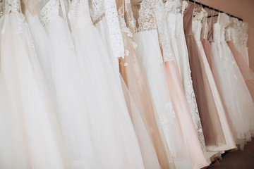 a close-up of skirts with a variety of white and pink wedding dresses with lush skirts that hang on a hanger against a pink wall background