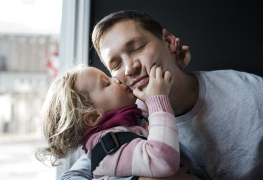
Daughter kissing father while sitting by window at home