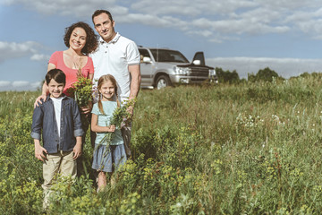 Happy together. Full length portrait of cheerful father and mother spending time with their kids on grassland. Girl is holding bouquet of wild flowers while boy is smiling. Copy space