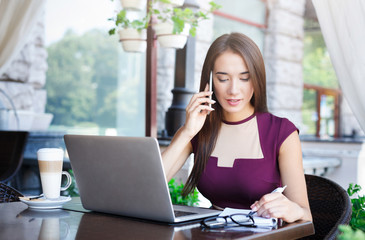 Young businesswoman talking on smartphone and making notes