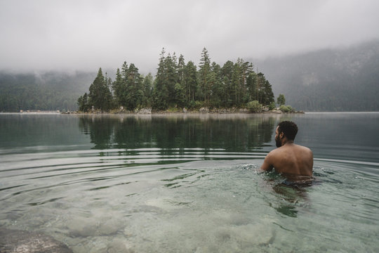 
Rear view of shirtless man swimming in lake at forest