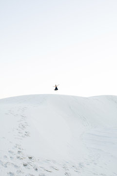 Distant view of woman jumping at White Sands National Monument against clear sky