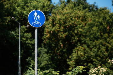 pedestrian bicycle zone in blue circle on background of green trees in park. city street sign concept. sign with person and child and bicycle in white and blue circle.