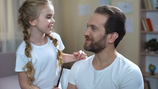 Little girl combing father hair and kissing cheek, playing games, family love