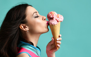 Young woman in pink hat eat strawberry ice-cream dessert in waffle cone on modern light blue 