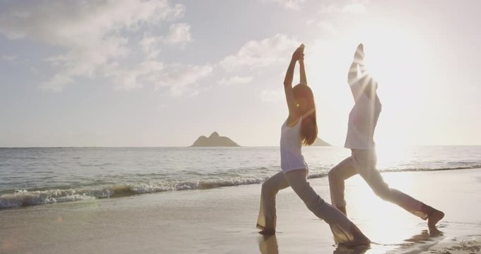 Yoga meditation and wellness lifestyle concept. People, man and woman doing yoga exercises on beach at sunrise on beautiful Warrior 1 pose. tion and yoga meditating on beach.