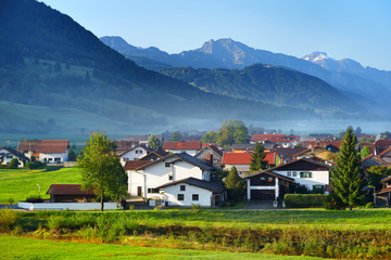 Breathtaking morning lansdcape of small bavarian village covered in fog. Scenic view of Bavarian Alps at sunrise with majestic mountains in the background.