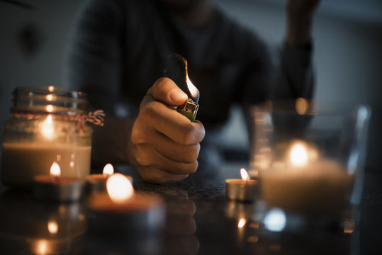 Midsection of man igniting candles with cigarette lighter on table in darkroom