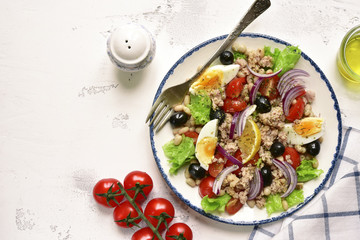 Tuna salad with white beans, tomatoes, boiled eggs and black olives.Top view with copy space.